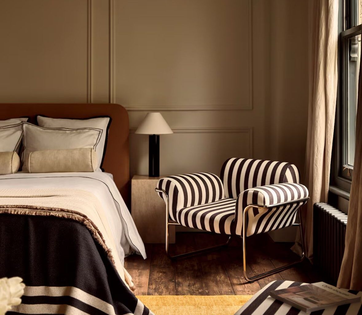 Contemporary bedroom featuring a black and white striped upholstered armchair with a tubular chrome frame, part of the 1970s striped interiors design revival in modern interior trends.
