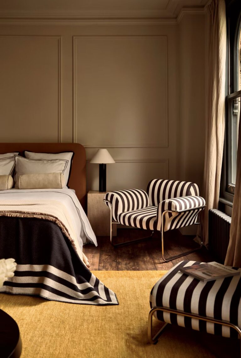 Contemporary bedroom featuring a black and white striped upholstered armchair with a tubular chrome frame, part of the 1970s striped interiors design revival in modern interior trends.