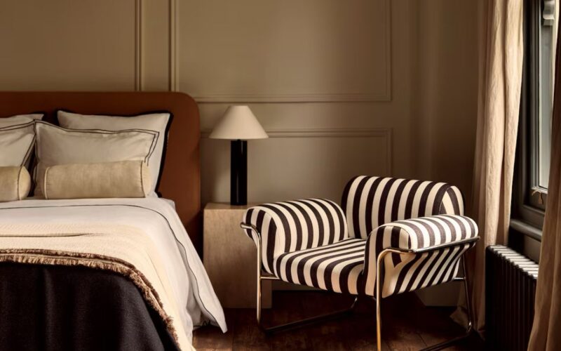 Contemporary bedroom featuring a black and white striped upholstered armchair with a tubular chrome frame, part of the 1970s striped interiors design revival in modern interior trends.